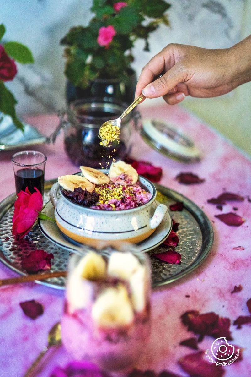 a hand drizzling chopped pistachio over a bowl of rose