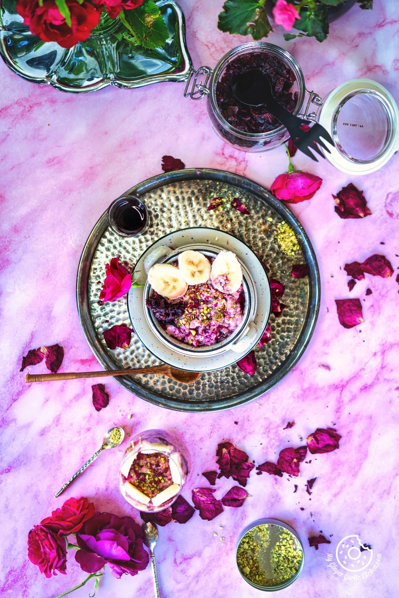 a pink table topped with a transparent glass filled with rose overnight oats and a bouquet of flowers in a glass vase