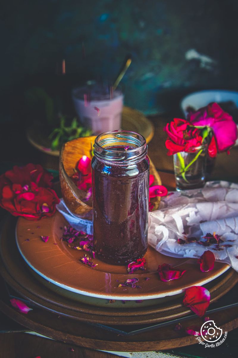 homemade rose syrup in glass bottle and fresh rose petals in background