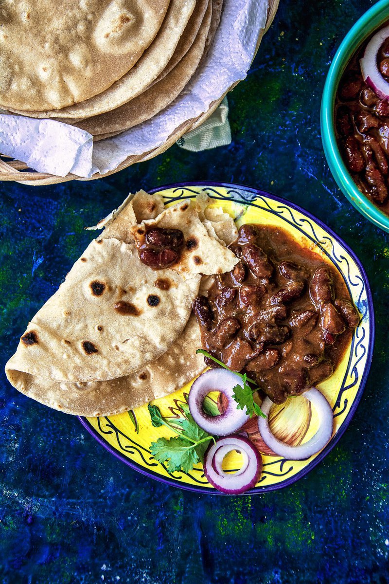 Plate of roti with kidney bean curry and sliced onions, with a side bowl of curry and blue textured background