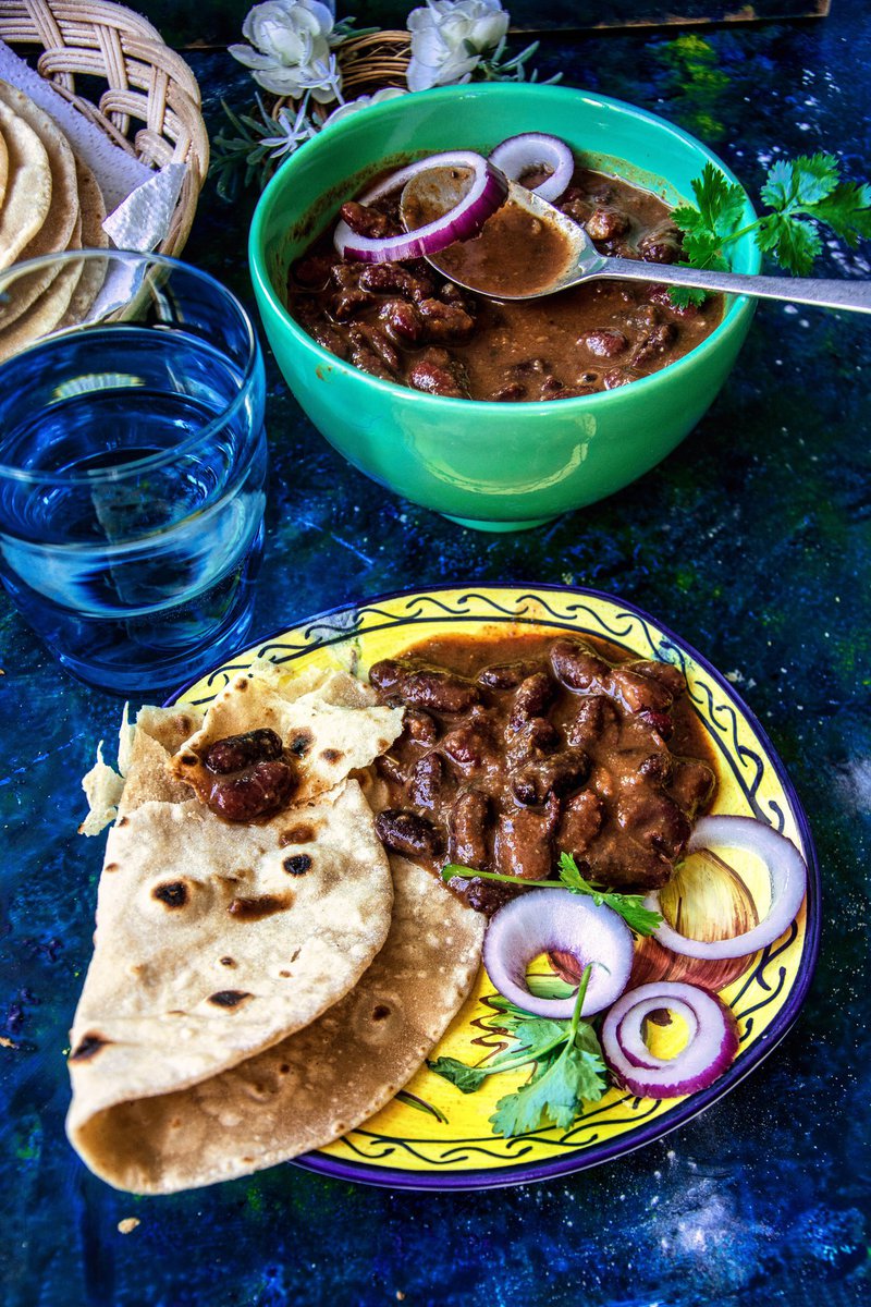 Close-up of a roti plate with kidney bean curry and sliced onions, with a water glass and curry bowl in the background