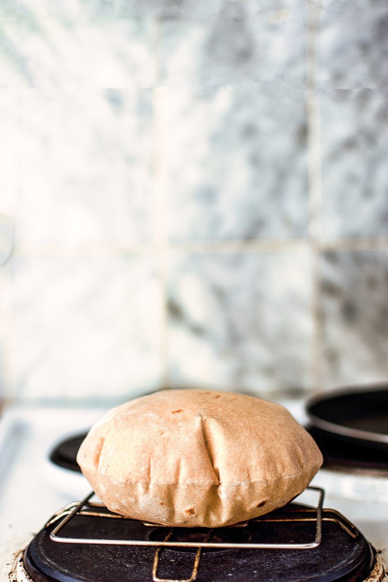 Puffed roti chapati on a gas stove burner with a tiled wall in the background