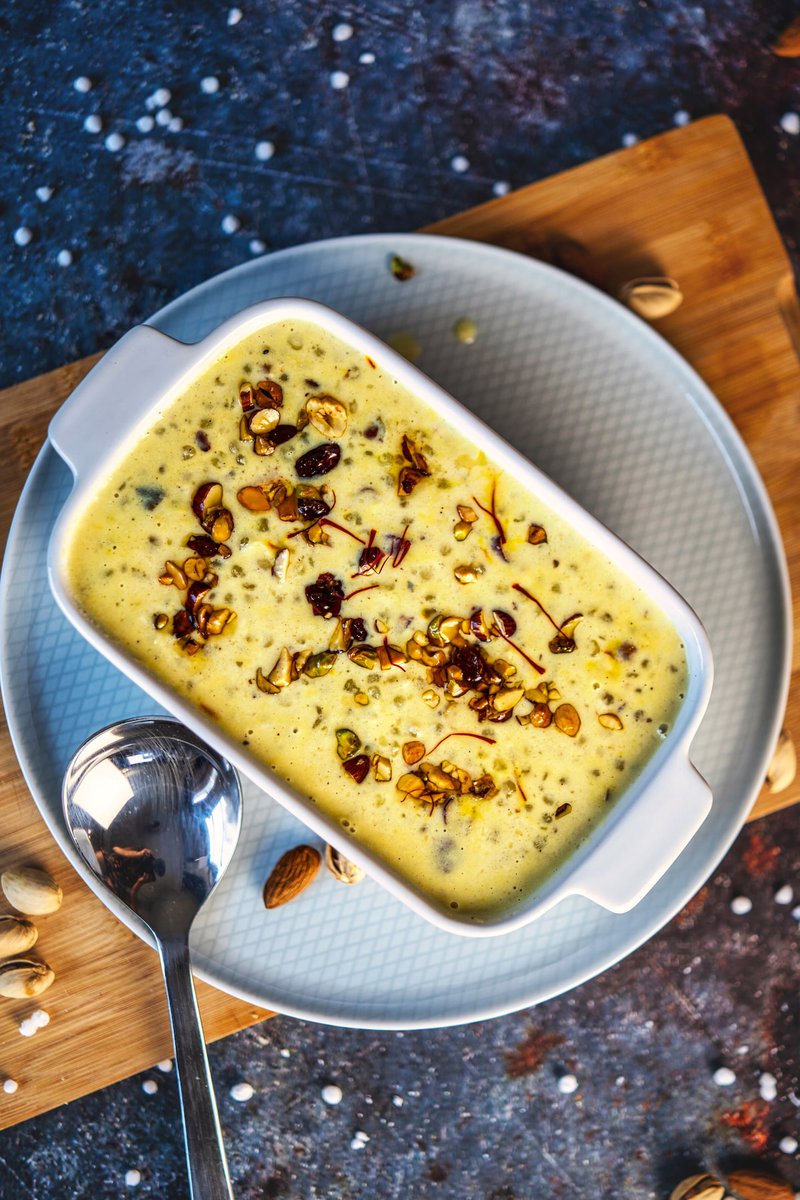 A dish of Sabudana Kheer garnished with nuts and saffron, served in a white rectangular bowl on a plate with a spoon.