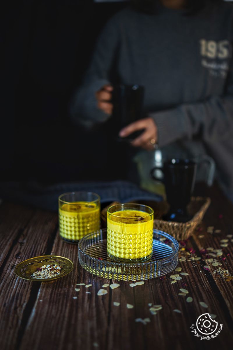 saffron milk in two transparent glasses and person holding a black cup in the background