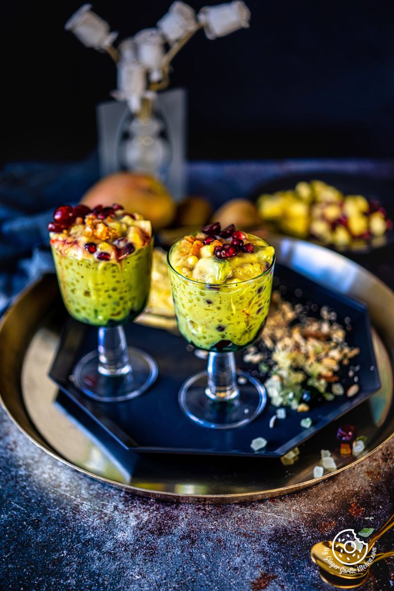 two sago fruit custard glasses on a metal plate and some chopped nuts on the side