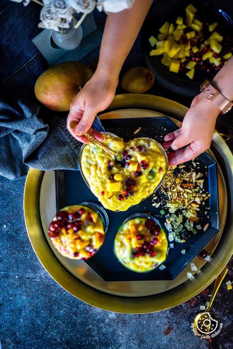overhead shot of two hands holding a heart shaped sago fruit custard bowl and two glasses on the side