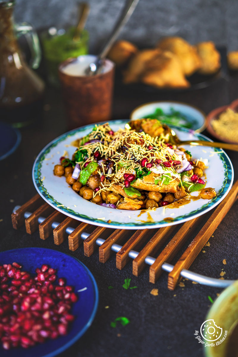 A delicious serving of samosa chaat on an intricately bordered plate, with a backdrop featuring Indian chai in a copper cup and savory snacks, capturing the essence of Indian cuisine.