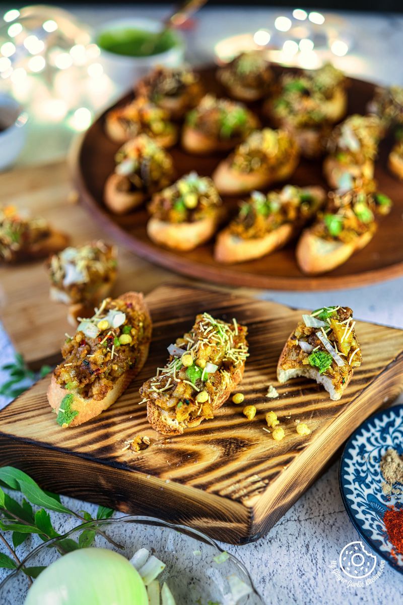 there are 3 Samosa Chaat Bruschetta appetizers on a wooden board on a table