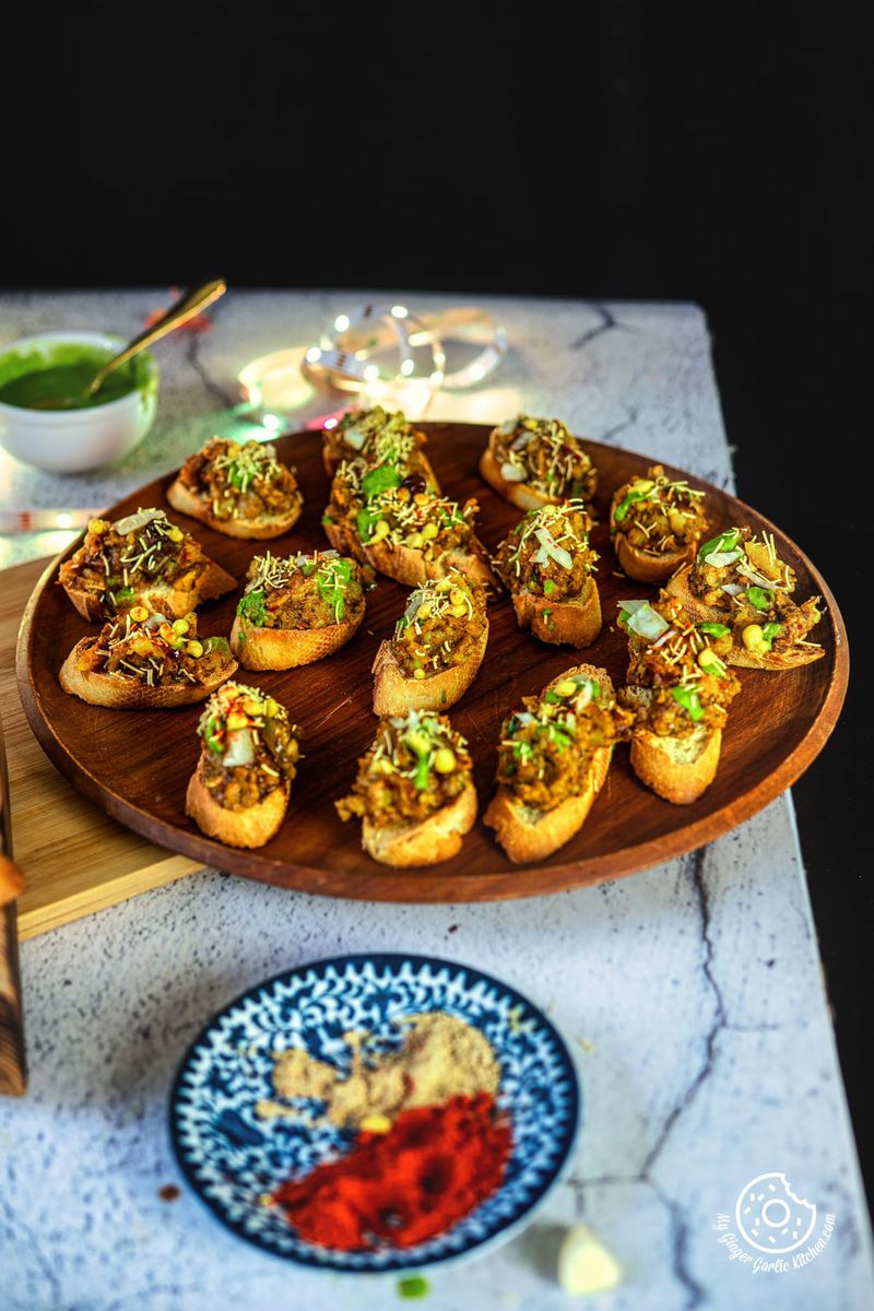 there are a plate of Samosa Chaat Bruschetta on a table with a bowl of green chutney'