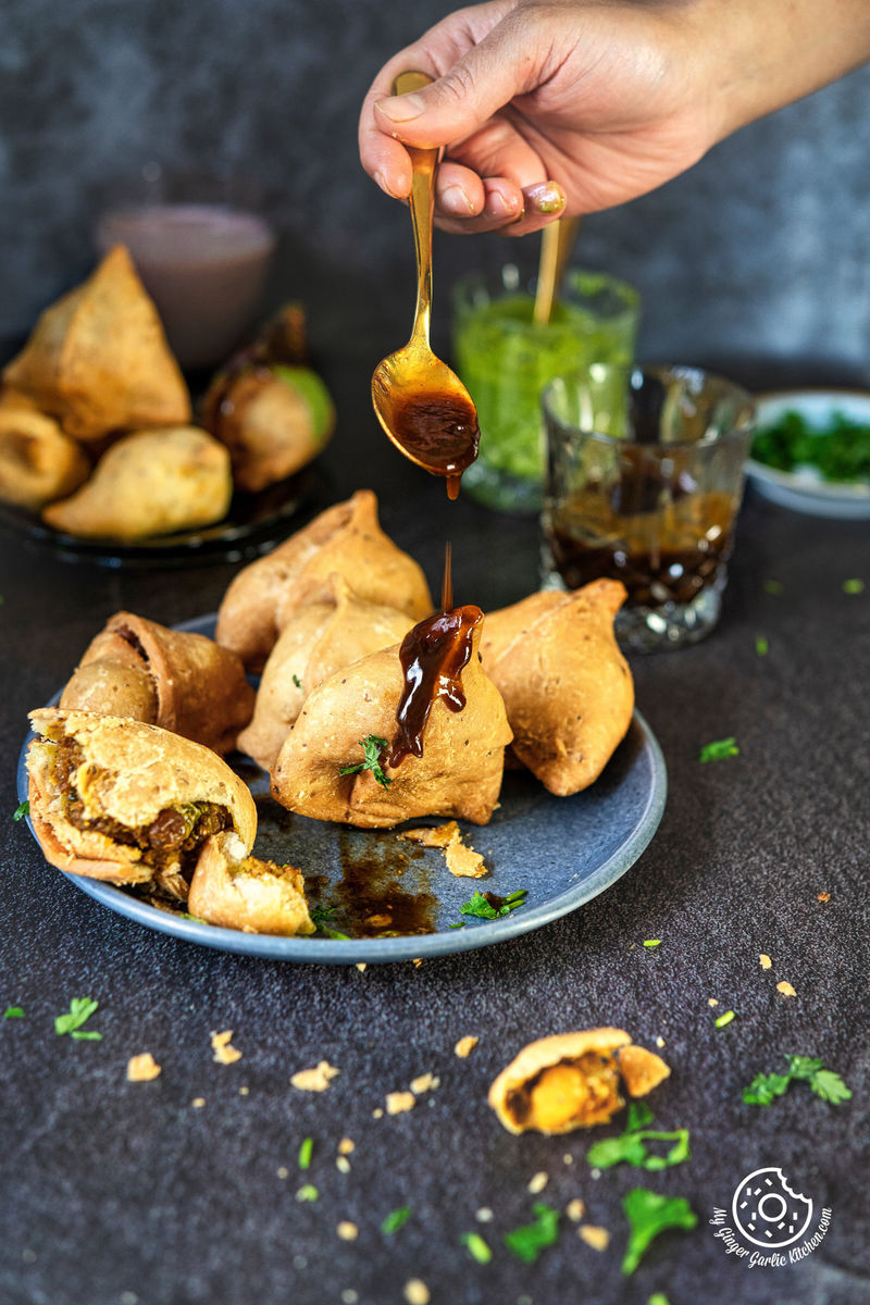 photo of a person dipping sauce onto a plate of samosa