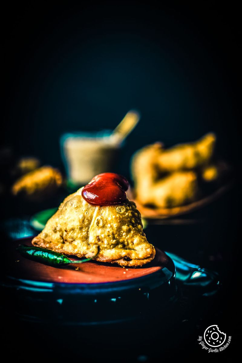 samosa topped with some ketchup and a green chili on the side