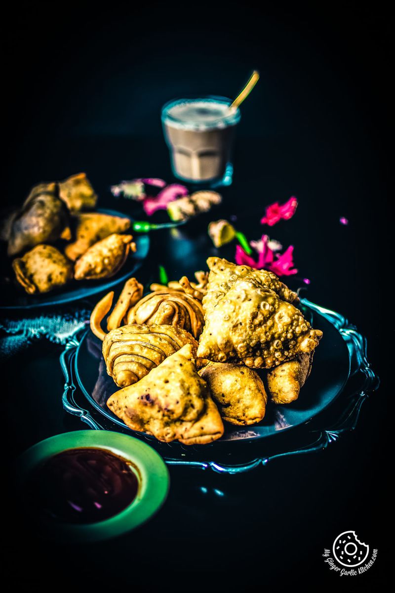 samosa served in plates and a cup of chai in the background