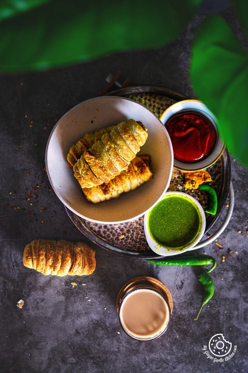 overhead photo of a plate of samosa roll with chutney bowls and a cup of coffee