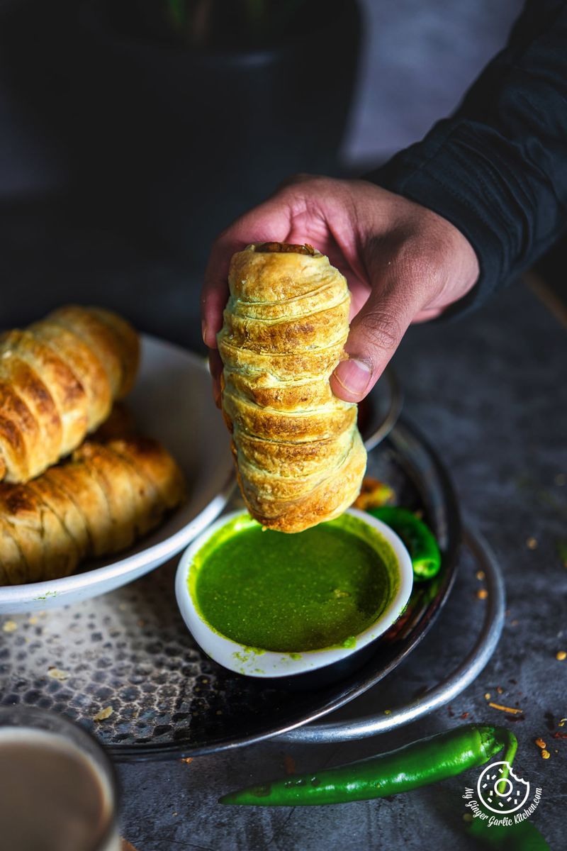 a person is putting a samosa roll into a bowl with green coriander chutney