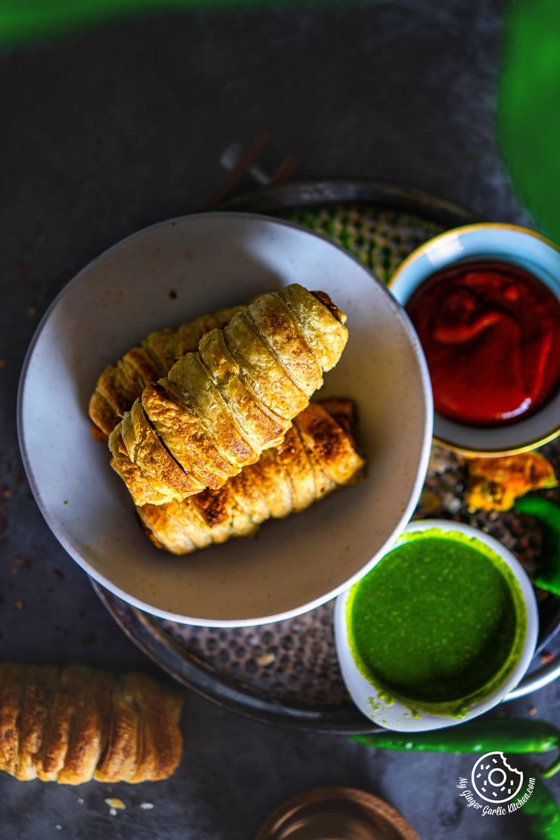 overhead closeup photo of a plate of samosa rolls with green coriander chutney and ketchup on the side