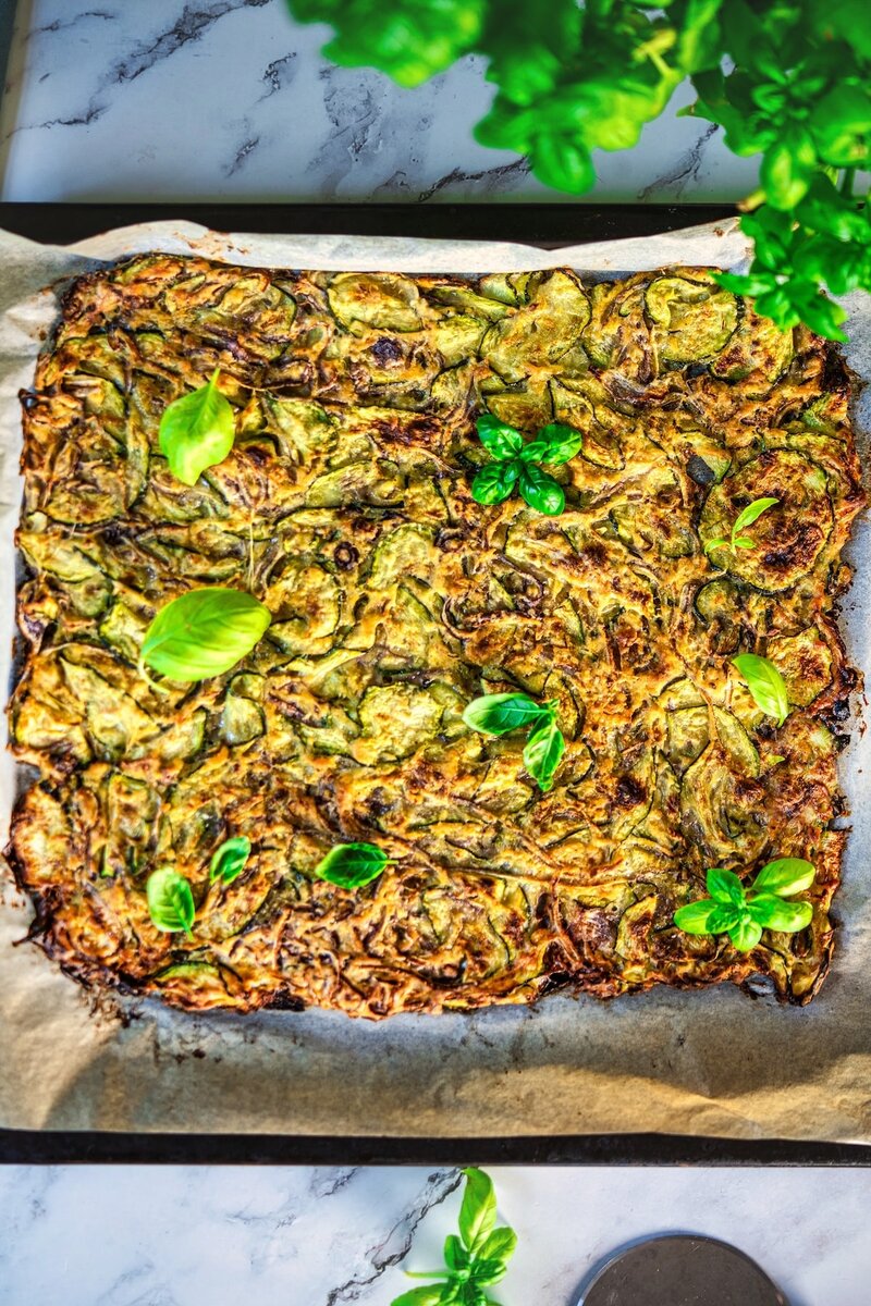 Authentic Tuscan scarpaccia zucchini tart baked on parchment, topped with fresh basil leaves