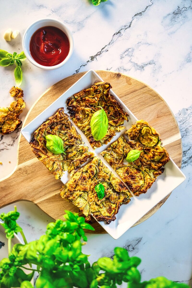 Crispy zucchini scarpaccia squares served with tomato dip and basil on rustic wooden board