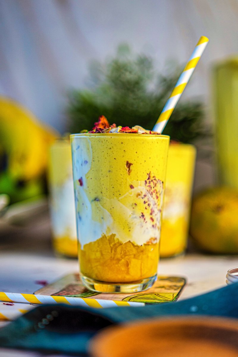 Close-up of a creamy saffron mango lassi served in a yogurt-lined glass with muddled mango chunks, rose petals, and chopped nuts.