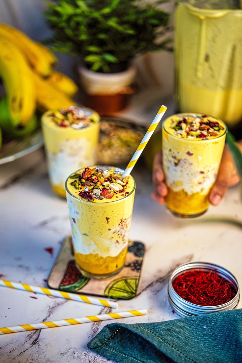 Homemade Shahi Mango Lassi served in decorated glasses with mango chunks, Greek yogurt, pistachios, almonds, rose petals, saffron, and edible silver leaf.