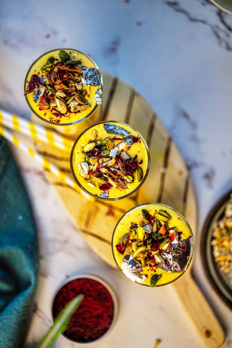 Top view of restaurant-style Shahi Mango Lassi garnished with nuts, dried rose petals, saffron strands, and edible silver leaf for a festive royal presentation.