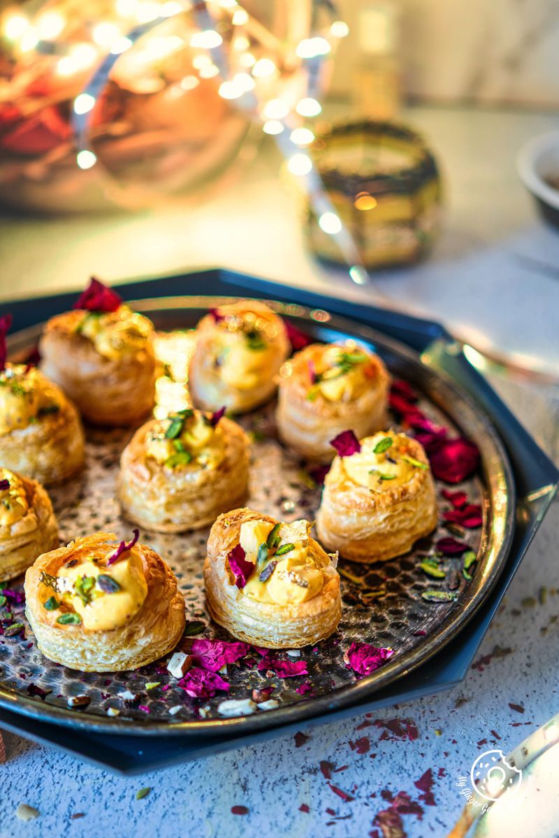 photo of a plate of shrikhand puff pastry cups with dried rose flowers on a table