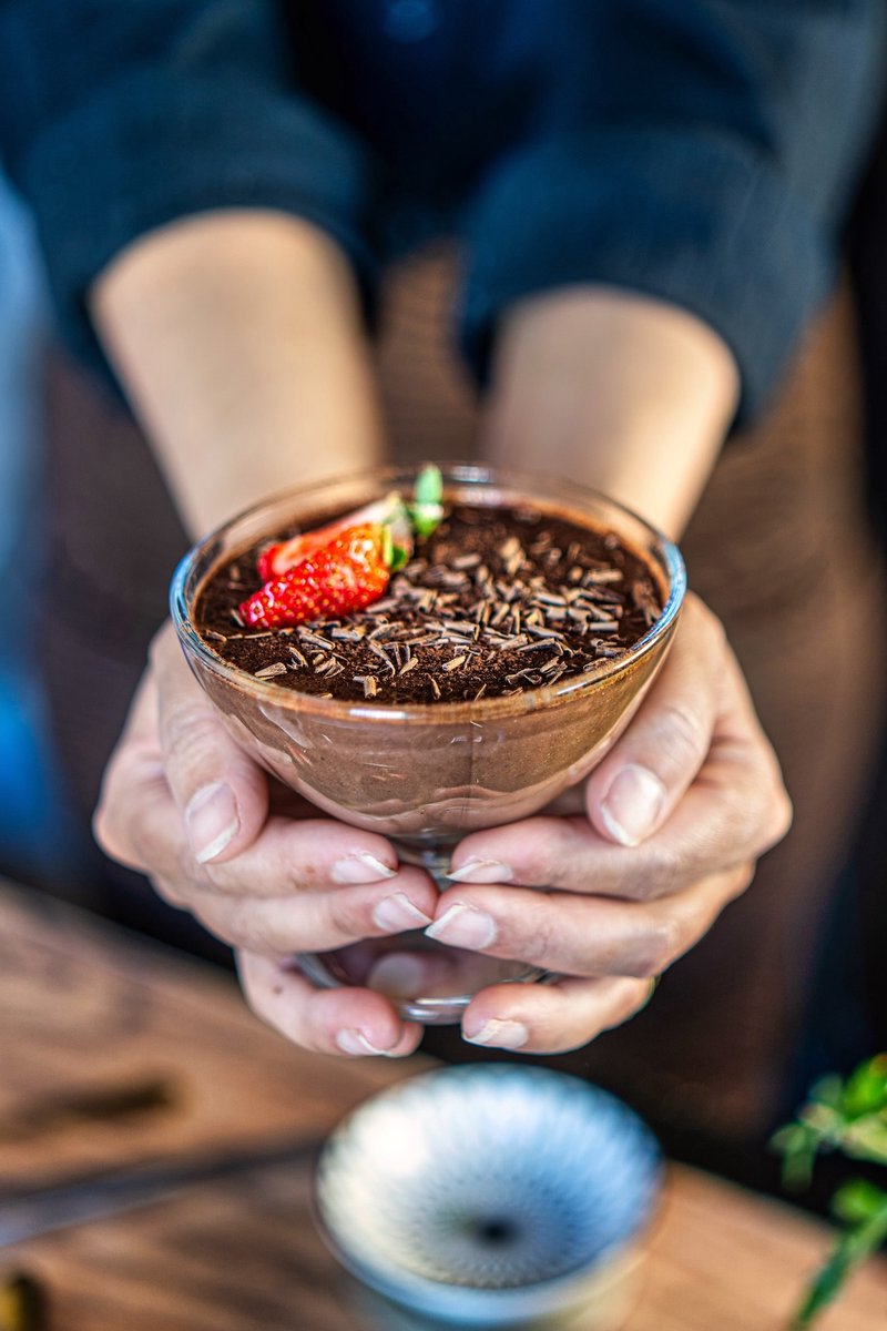 Creamy vegan silken tofu chocolate pudding held in hands and topped with strawberries and chocolate shavings