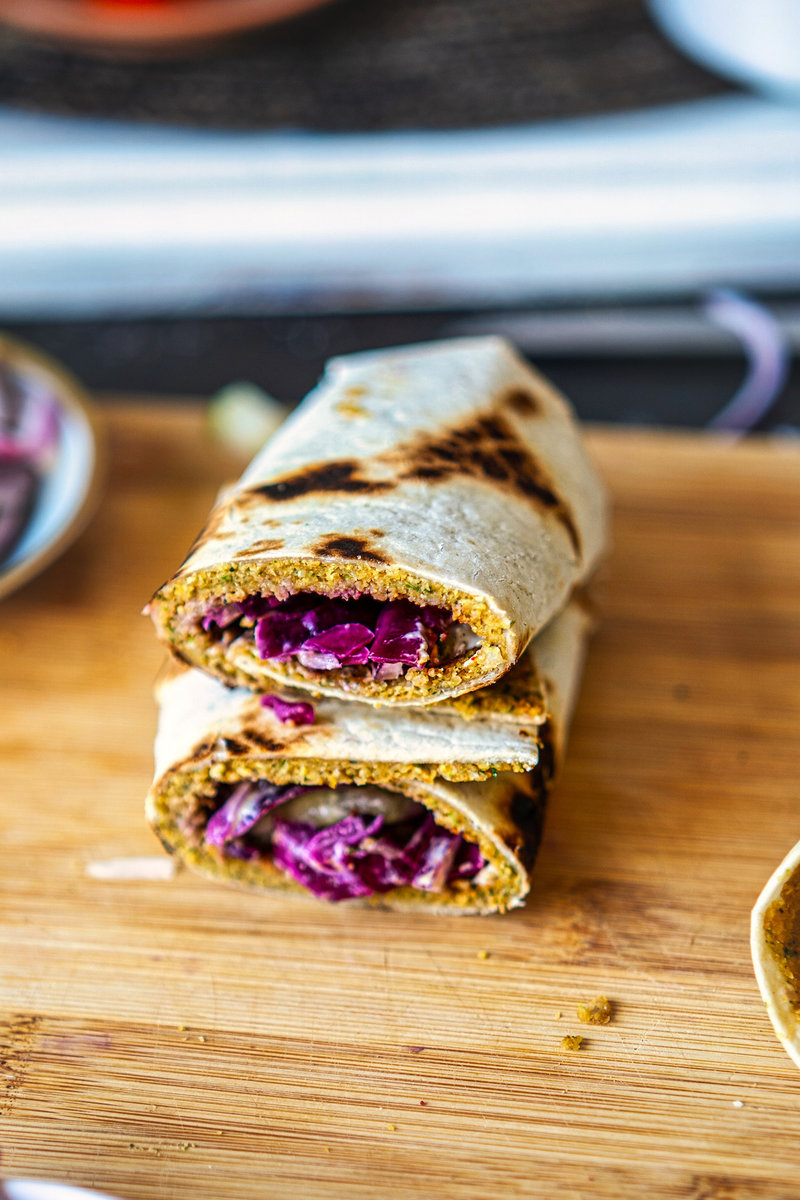 Smashed falafel wraps filled with vibrant red cabbage on a wooden cutting board.