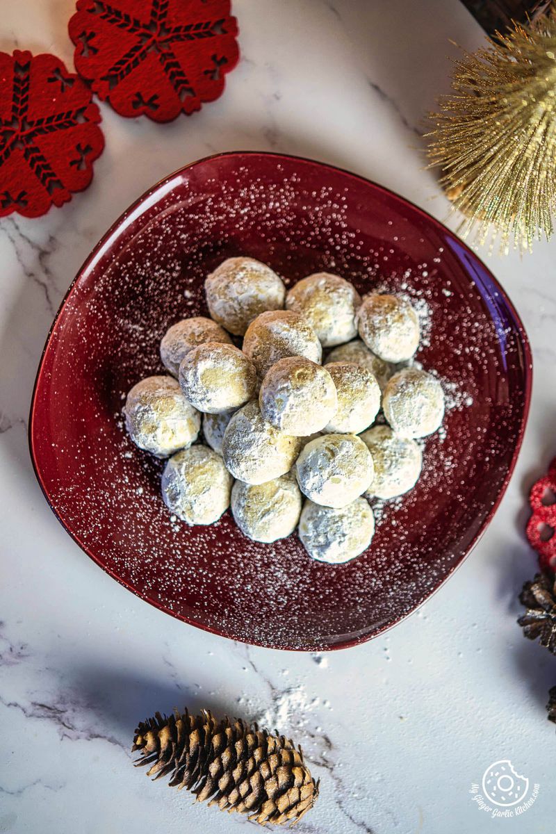 a red plate filled with sugared snowball cookies and pine cones on a white table