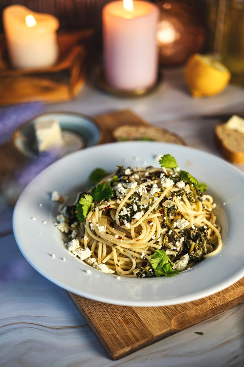 Close-up of spinach pasta with feta cheese and fresh herbs, garnished with candles in the background.