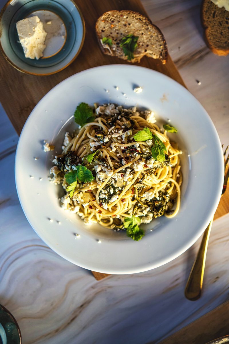 Overhead shot of creamy spinach feta pasta on white plate, garnished with parmesan and herbs, served with bread and butter on marble surface