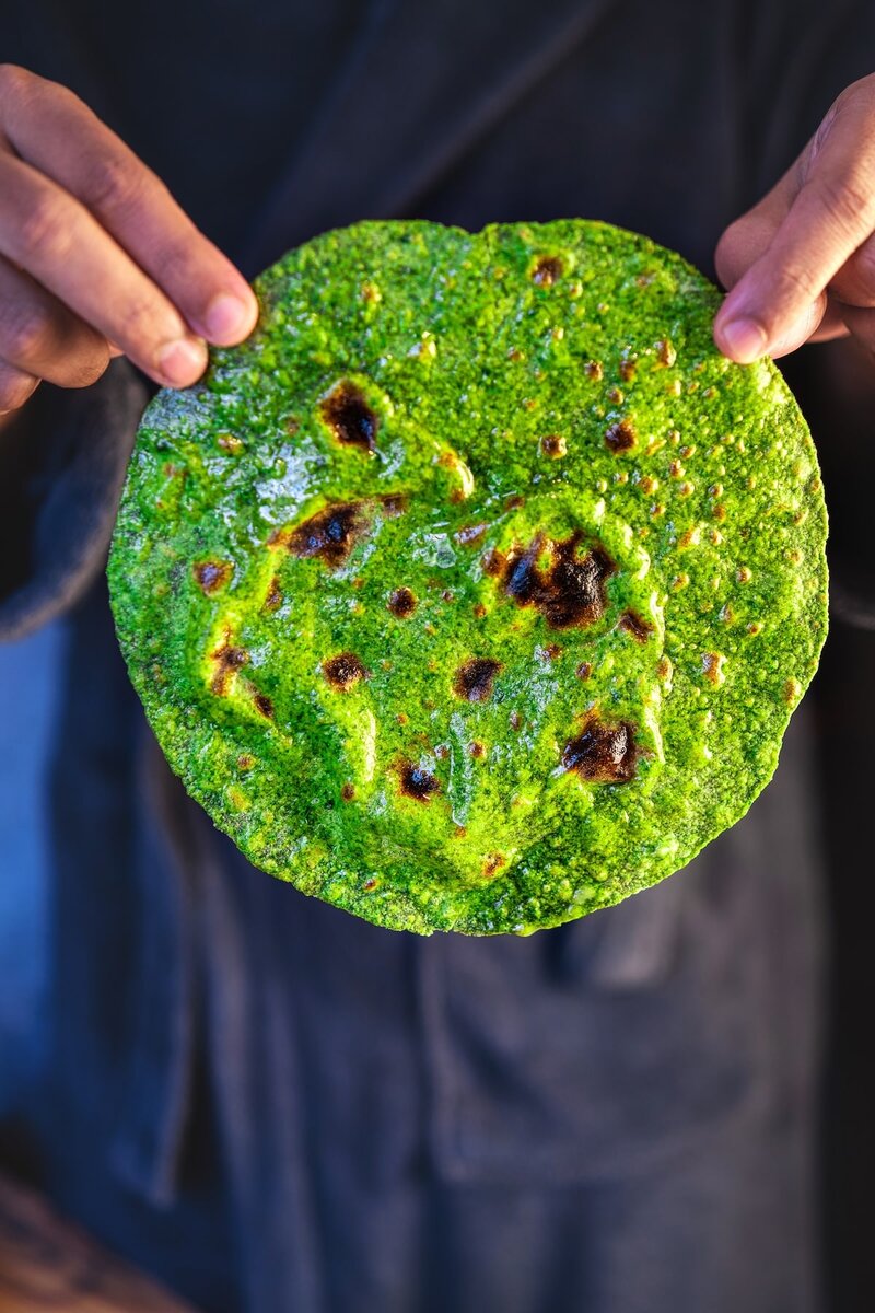 Soft spinach roti held in hands, naturally green palak roti with golden spots and brushed with ghee