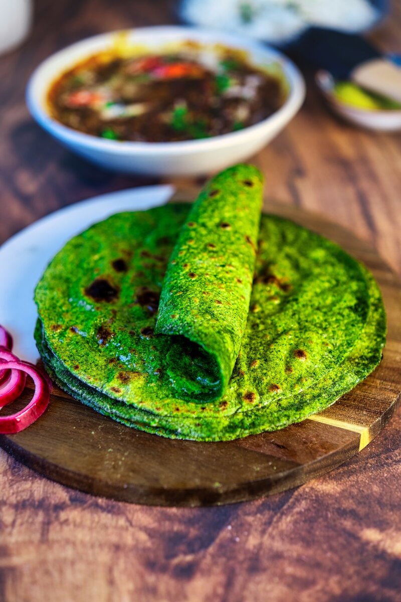 Folded spinach roti on a plate, soft green palak chapati served with Indian curry