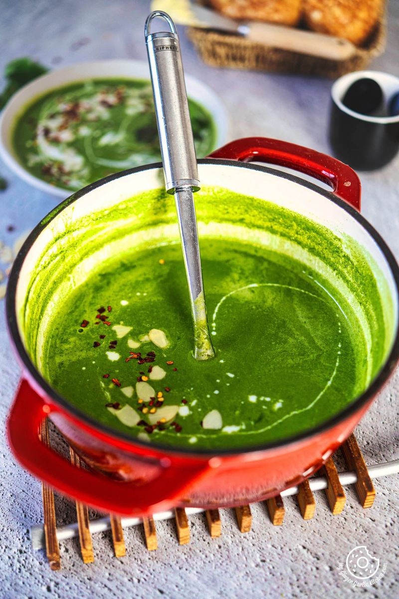 a red pof of green spinach soup with a spoon in it