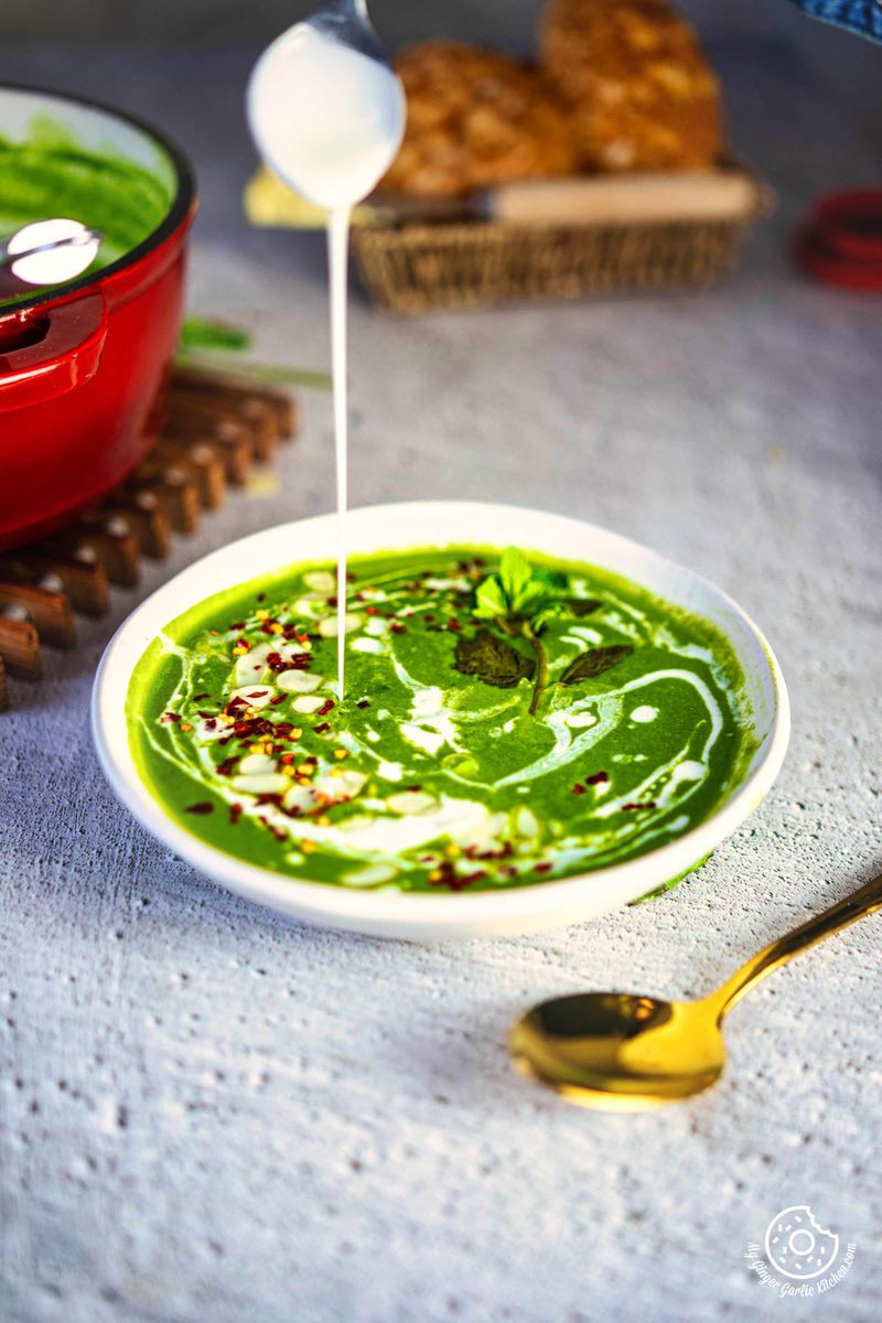 a person is pouring milk into a bowl of spinach soup