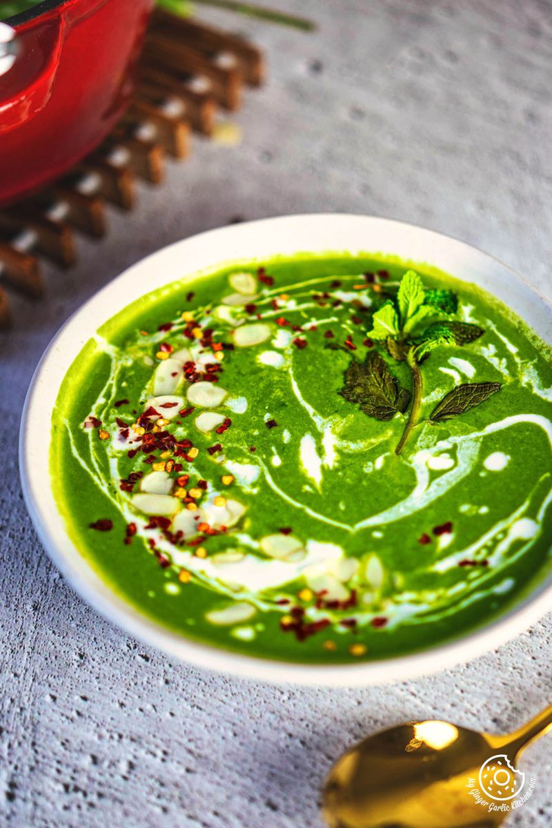 closeup photo of a bowl of spinach soup on a table with a spoon and a bowl of soup next to it