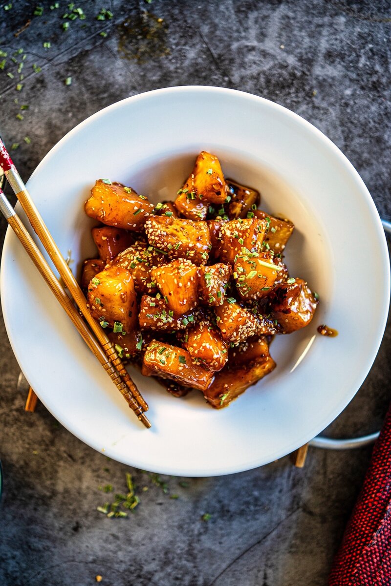 Sweet and spicy sticky chili garlic pineapple served in a bowl with sesame seeds and chives, easy 10-minute pineapple recipe