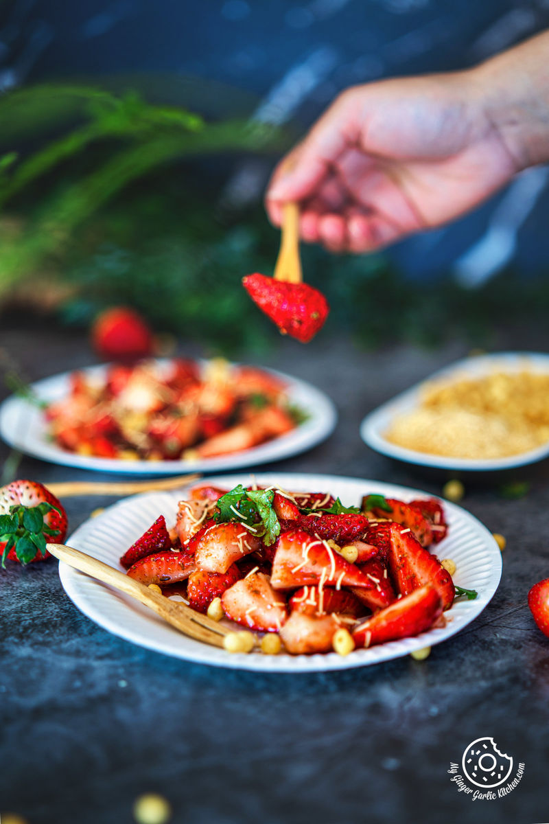 photo of a person is dipping a strawberry onto a plate of strawberry chaat