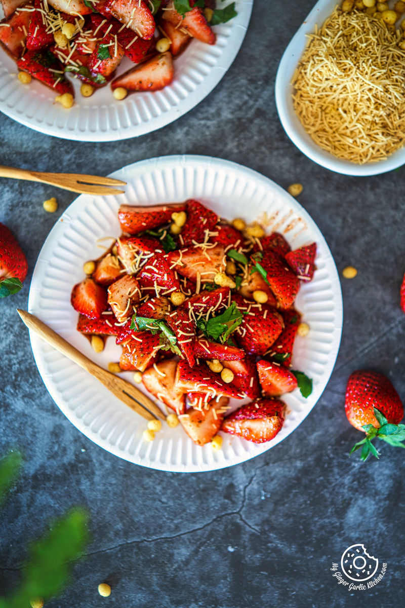 overhead photo of two plates of strawberry chaat with strawberries and sev noodles on them