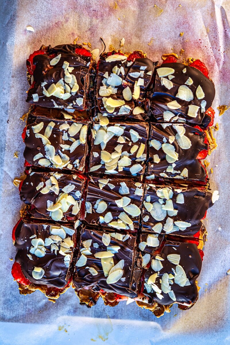 Strawberry chocolate date bark cut into squares topped with almond flakes on parchment paper