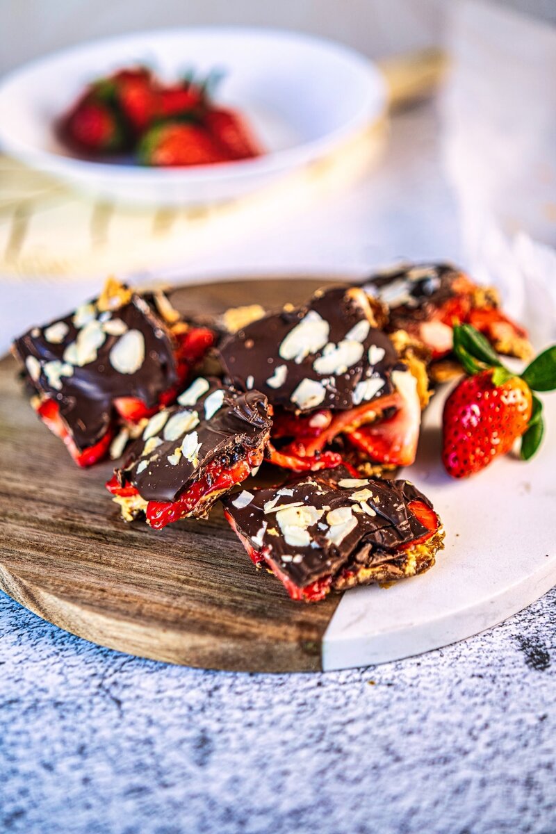 Strawberry chocolate date bark pieces served on a wooden board with fresh strawberries on the side