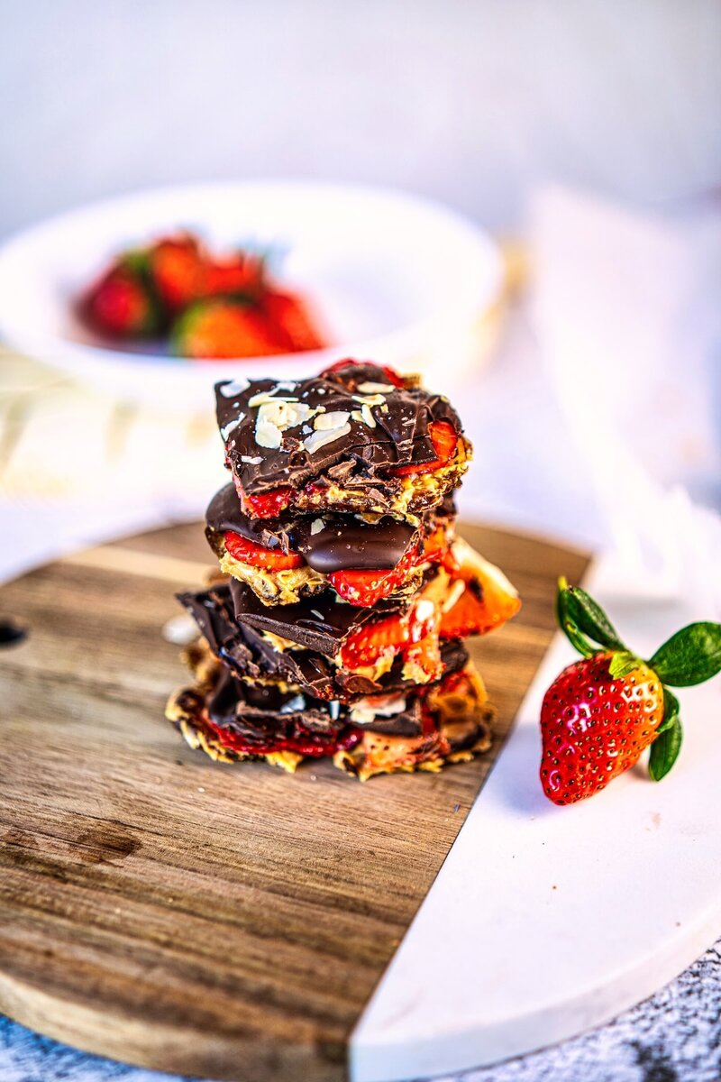 Stacked strawberry chocolate date bark pieces on a wooden board with fresh strawberries