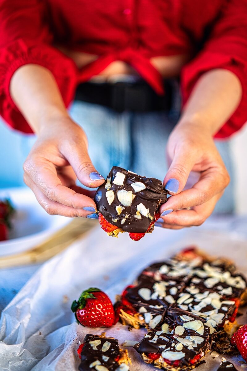 Hand holding a piece of strawberry chocolate date bark showing layers of dates, peanut butter, and chocolate