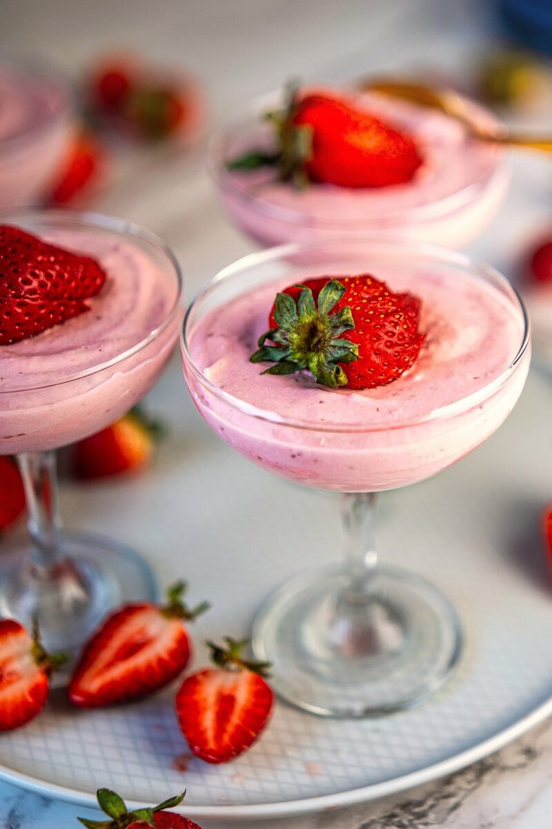 Close-up of three glasses of strawberry mousse, each garnished with a whole fresh strawberry, with halved strawberries around them on a tray.