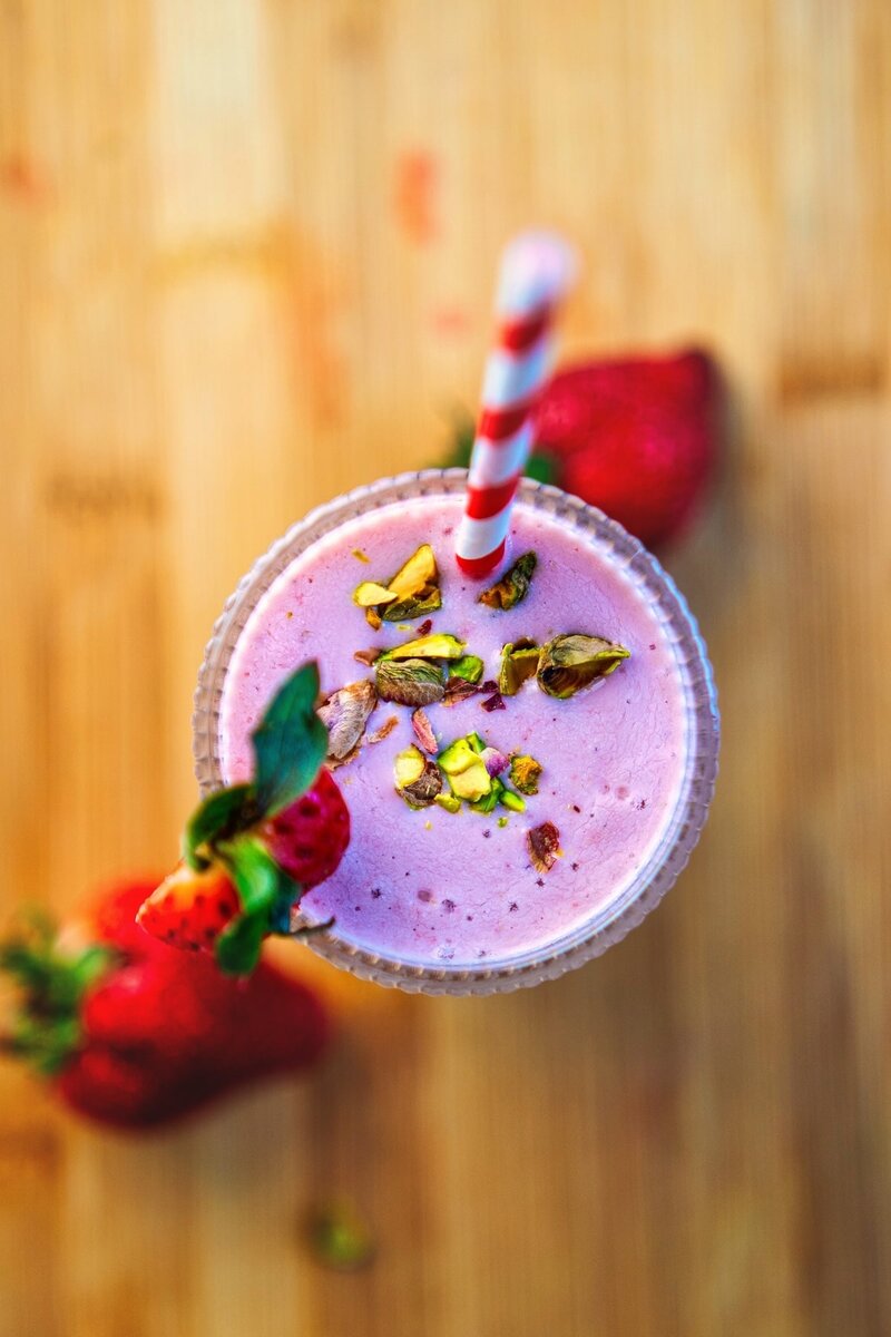 Overhead view of pink strawberry smoothie bowl garnished with crushed pistachios and striped straw