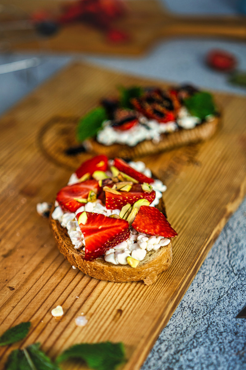 Close-up view of strawberry cottage cheese toast with fresh strawberry slices and pistachio toppings on a wooden cutting board.