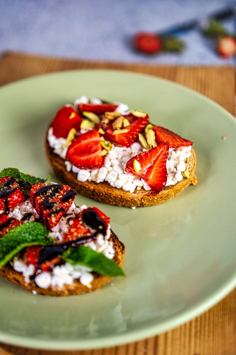 Angled view of strawberry cottage cheese toast showcasing fresh strawberry slices and pistachio toppings on a green plate.