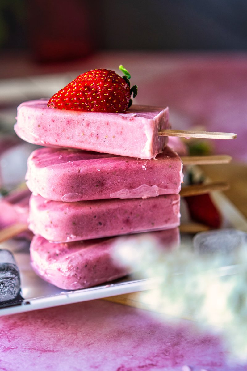 Stack of strawberry creamsicles with a fresh strawberry on top, set on a white tray next to ice cubes.