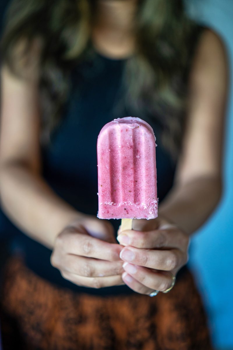 A person holding a strawberry creamsicle with a blurred background emphasizing the vibrant pink color of the popsicle.