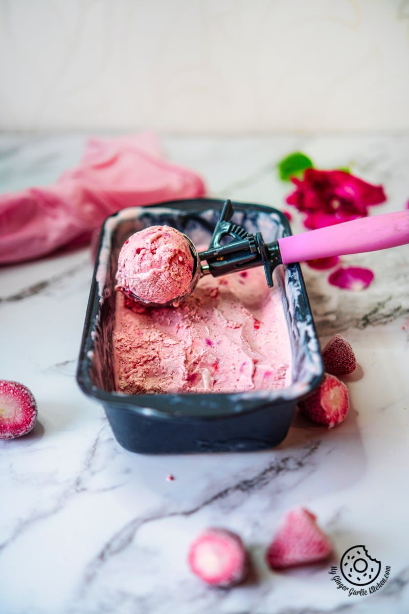 homemade strawberry ice cream in a container and an ice cream scoop
