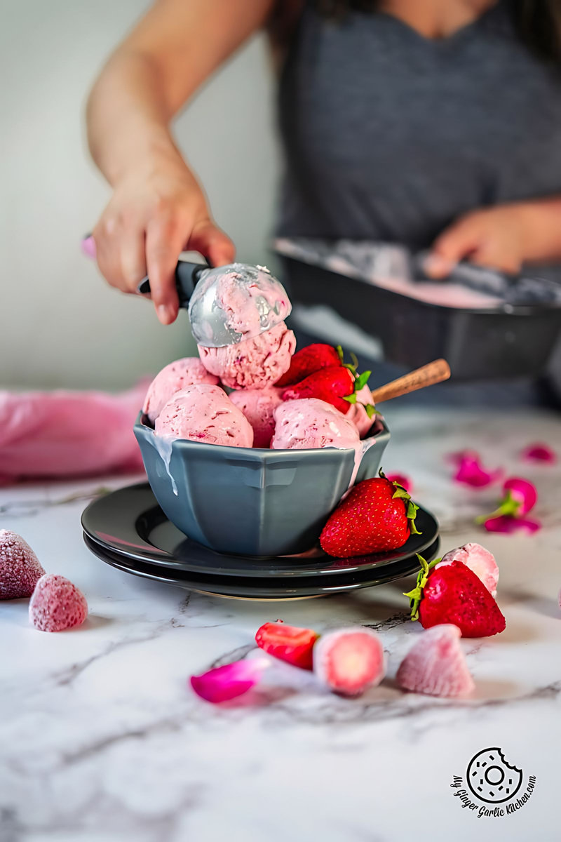 strawberry ice cream in a grey bowl and a female holding a spoon with strawberry ice cream in the background